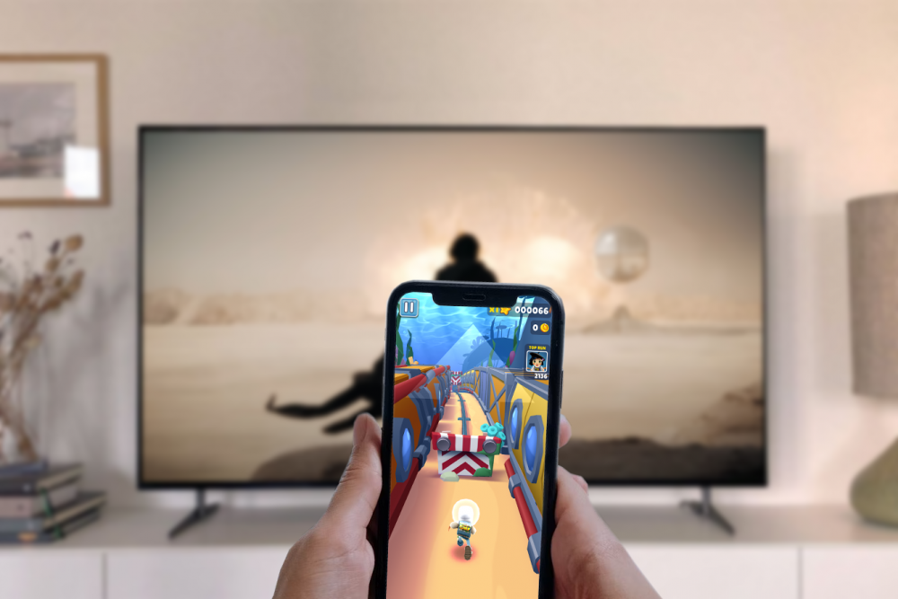 Ett par händer håller i en telefon med Subway Surfers på, medan Dune: Part II visas på en TV i bakgrunden.
